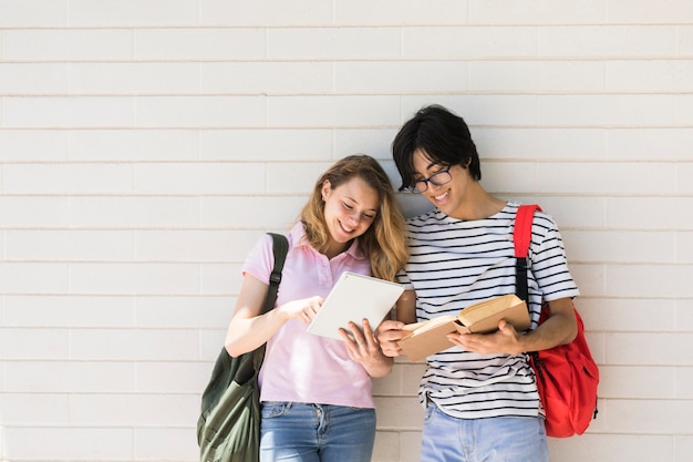 Foto par multirracial, usando, tabuleta, e, livro leitura, contra, branca, parede