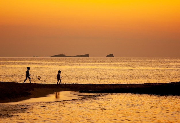 un par de niños jugando en una playa al atardecer