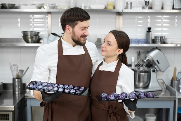 Un par de pasteleros amorosos, un hombre y una mujer, abrazan y sostienen una decoración de pastel de chocolate