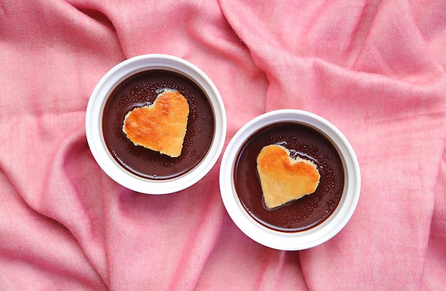 Par de pasteles de mousse de chocolate negro con pasteles de gasa en forma de corazón sobre tela rosa para cortinas