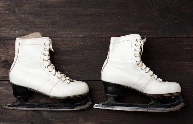 Par de patines de cuero blanco para patinaje artístico sobre madera marrón