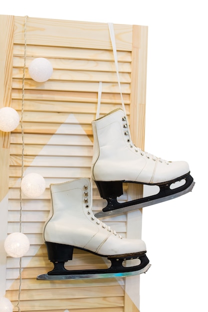 Par de patines femeninos colgando de cordones en la puerta de madera o madera con decoración de bolas de nieve en invierno Navidad o vacaciones de año nuevo aislado sobre fondo blanco.