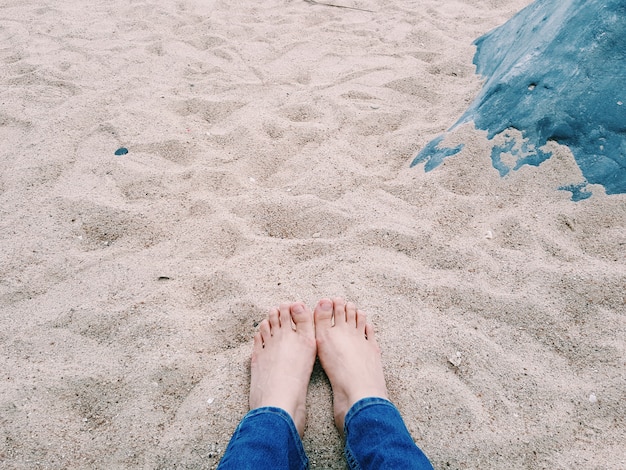 Un par de pies de una dama asiática descansan en la playa de arena y se sientan cerca de una roca con copia spac