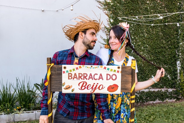 Un par de pueblerinos con sombreros de paja mirándose enamorados en un festival de junio en Brasil Traducción Carpa de besos