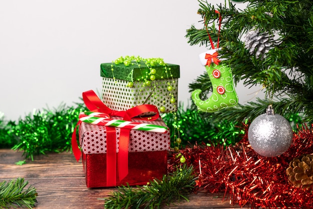 Un par de regalos envueltos en brillantes envases festivos, junto a los cuales se encuentra una piruleta brillante en forma de bastón, ubicada en una mesa de madera junto al árbol de Navidad.