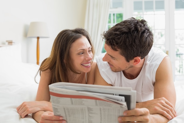 Par relajado leyendo periódico en la cama