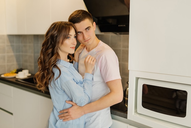 Par romântico em casa. Mulher jovem e atraente e homem bonito estão aproveitando a passar tempo juntos em pé na cozinha moderna luz. Conceito de relacionamento.