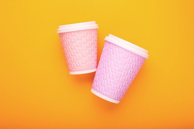 Par de vasos de café de cartón rosa sobre un fondo amarillo