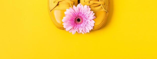 Par de zapatillas amarillas y flor de gerbera rosa Banner mínimo con lugar para texto
