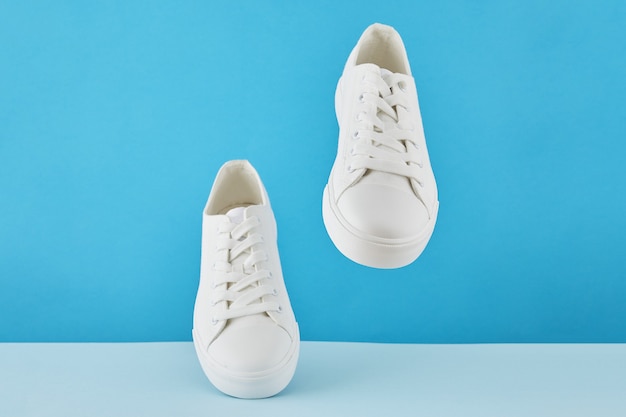 Par de zapatillas blancas con estilo de moda, zapatillas deportivas para correr sobre un fondo azul pastel.