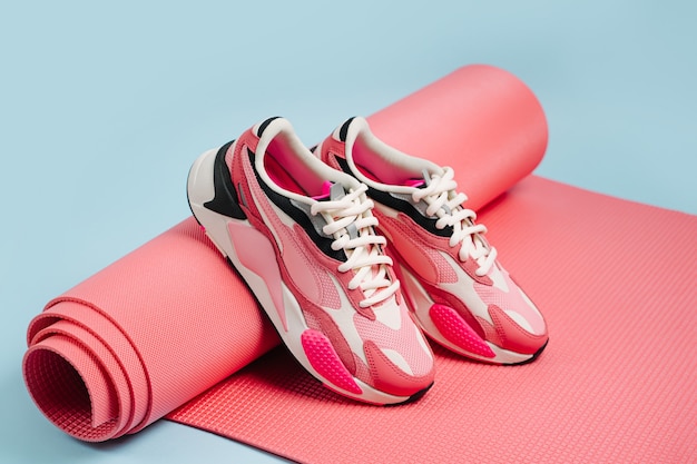 Par de zapatillas de mujer con tapete de yoga rosa sobre fondo azul. Concepto de blog o revista de moda. Estilo de vida saludable. Entrenamiento en casa.