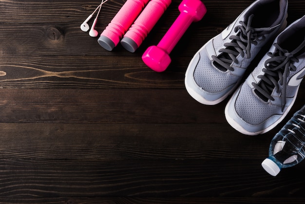 Par de zapatos deportivos, auriculares, pesa y botella de agua en la mesa de madera negra