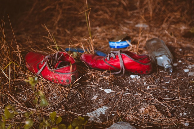 Un par de zapatos rojos están tirados en el suelo con una botella de cerveza en el fondo.