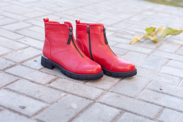 Un par de zapatos rojos de mujer se paran en las baldosas en el otoño.