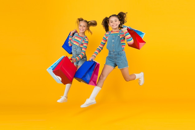 Para a compra. Moda moderna. Moda infantil. Crianças fofas se apressam para a temporada de vendas. Desconto e venda. As meninas carregam sacolas de compras. Roupas combinando. Moderno e chique. Loja de moda.