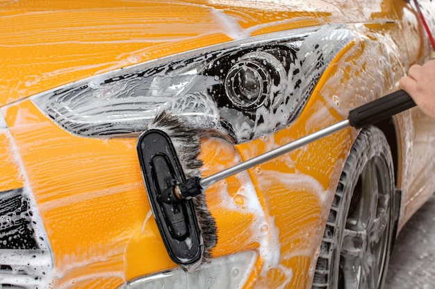 Para-choque dianteiro e luz de um carro amarelo lavado em autosserviço, escova deixando traços brancos.