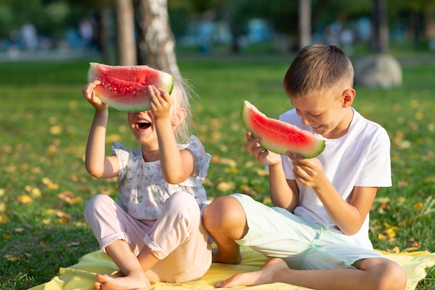 Para crianças fofas lttle menino e menina comendo melancia suculenta no piquenique no outono Park Prado.