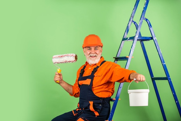 Foto para fazer reparos homem em roupas de trabalho pintando parede em quarto vazio pintor de macacão e boné com balde de tinta construtor trabalhador pintura fachada trabalhos de isolamento térmico escadaria de homem pintor