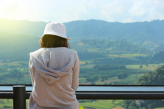 Para trás da menina asiática que senta e que presta atenção a uma vista natural.