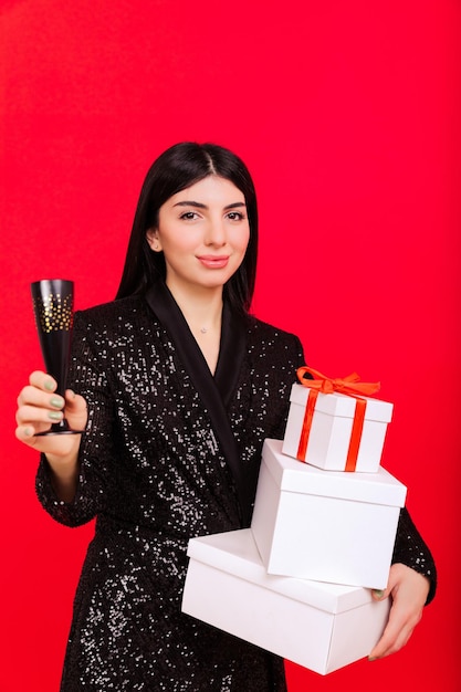 Parabéns aos colegas no Natal Uma jovem com presentes e uma taça de champanhe em um fundo vermelho