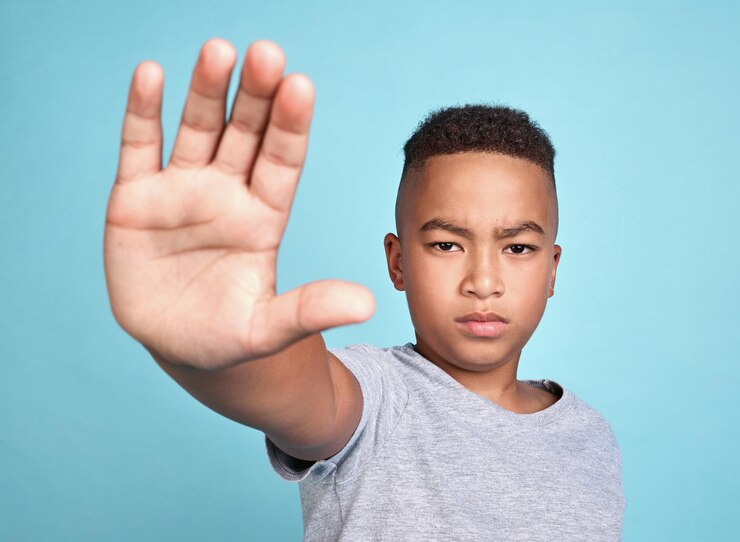 Foto parada de mão e crianças com um menino no estúdio em um fundo azul contra bullying, abuso ou violência crianças direitos humanos e empoderamento com uma criança do sexo masculino tomando uma posição para a nossa juventude