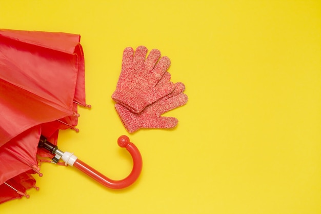 Paraguas y guantes rojos para niños sobre un fondo amarillo con espacio para copiar