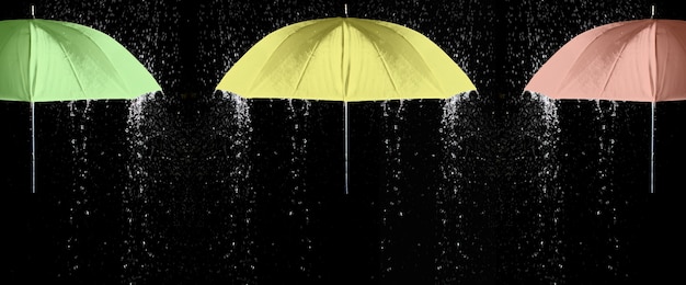 Paraguas verdes, amarillos y rojos bajo gotas de lluvia con fondo negro. Concepto de negocio y moda.