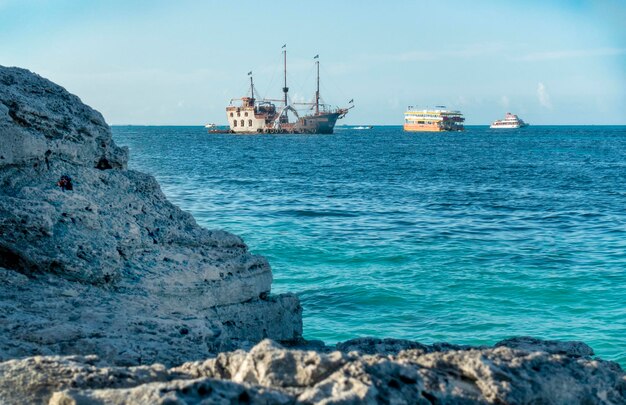 Foto paraíso tropical vista do oceano azul brilhante com velhos navios e iates vintage e grande costa rochosa