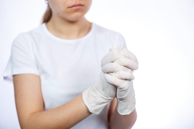 Paramédico de garota calça luvas médicas brancas nas mãos. proteção contra germes e vírus. ela está com uma camiseta branca sobre um fundo branco.