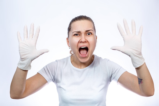 Paramédico de garota calça luvas médicas brancas nas mãos. Proteção contra germes e vírus. Ela está com uma camiseta branca sobre um fundo branco.