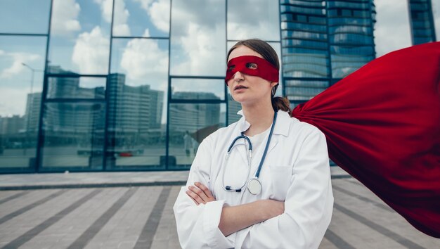 Paramédico femenino en un impermeable de superhéroe de pie en una calle de la ciudad. foto con espacio de copia.