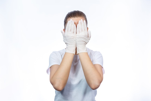 El paramédico de la muchacha se pone los guantes médicos blancos en las manos. Protección contra gérmenes y virus. Ella está en una camiseta blanca sobre un fondo blanco.