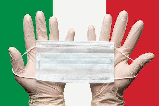 Paramédico sosteniendo mascarilla respiratoria en dos manos con guantes blancos en la bandera de fondo de Italia