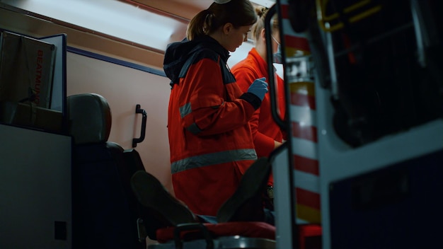 Foto paramedicos de ems resgatando paciente em carro de emergência médicos do sexo feminino tratando homem em macas trabalhadores médicos salvando a vida da vítima luzes azuis e vermelhas da ambulância piscando à noite conceito de resgate