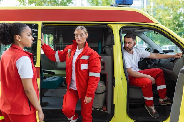 Paramédicos e médico em pé na ambulância lateral Médico está carregando uma bolsa de trauma médico Grupo de três paramédicos em frente à ambulância com sorriso