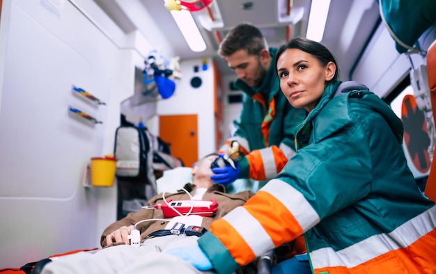 Foto los paramédicos están trabajando con un paciente mayor mientras está acostado en una camilla en una ambulancia.