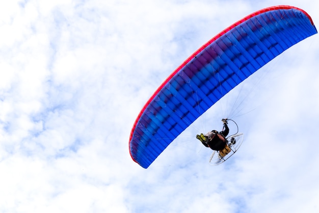 Parapente de motor volando en el cielo azul con nubes blancas