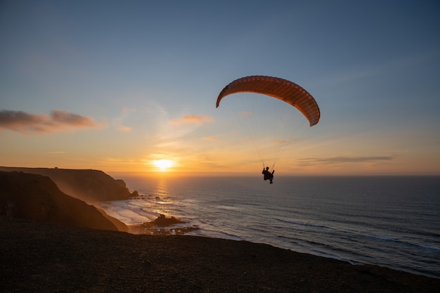 Parapente que voa sobre a costa do mar no por do sol. esporte de parapente