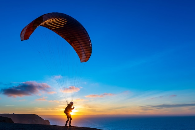 Parapente que voa sobre a costa do mar no por do sol. Esporte de parapente