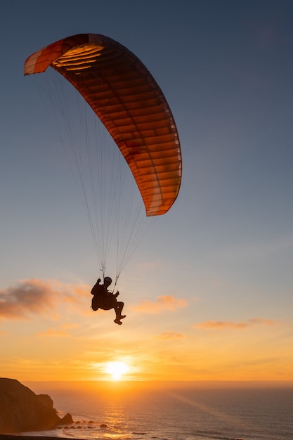 Foto parapente que voa sobre a costa do mar no por do sol. esporte de parapente
