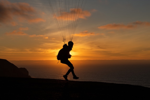 Parapente que voa sobre a costa do mar no por do sol. Esporte de parapente