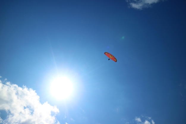 Parapente rojo volando en el cielo azul con el sol deslumbrante