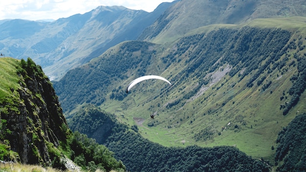 Parapente voando sobre montanhas durante o dia de verão - Geórgia, Kazbegi