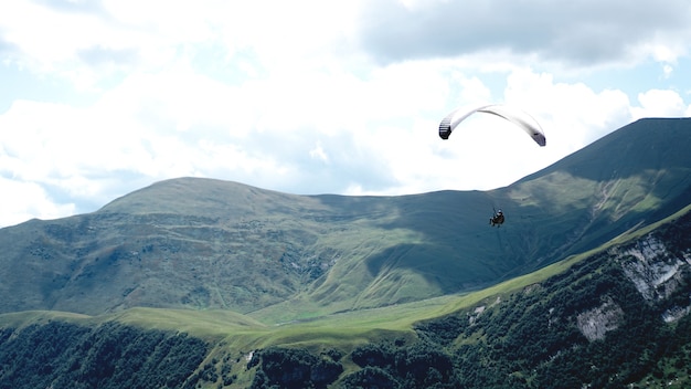 Parapente voando sobre montanhas durante o dia de verão - geórgia, kazbegi