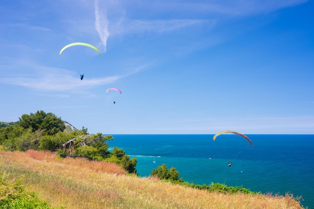 Parapentes sobrevolando la costa escénica de la Italia natural de Conero Deporte extremo sobre la espectacular punta de la costa en el destino turístico del mar Mediterráneo