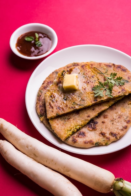 Paratha recheado com Daikon ou Rabanete ou Mooli servido em prato com manteiga e ketchup de tomate, sobre fundo colorido ou de madeira. foco seletivo