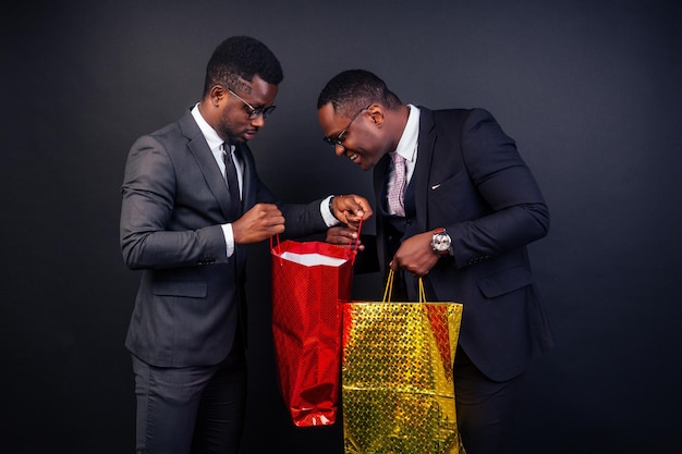 Parceiros de negócios masculinos afro-americanos segurando sacolas de compras em um fundo preto no estúdio. conceito sazonal de venda de sexta-feira negra