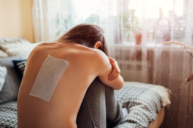 Parche para aliviar el dolor de espalda Triste mujer aplicó yeso en el omóplato en casa que sufre de dolor de columna