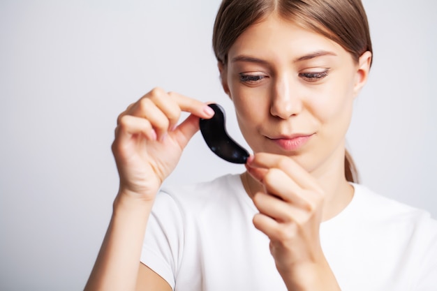 Parche en el ojo, hermosa mujer con maquillaje natural y parches negros en gel para ojos en piel facial