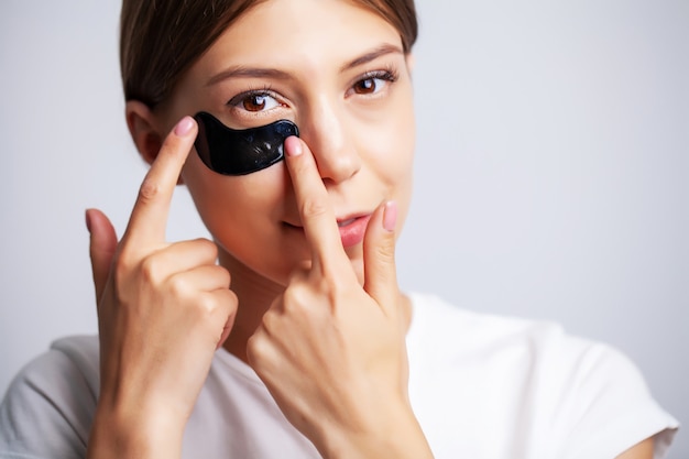 Parche en el ojo, hermosa mujer con maquillaje natural y parches negros en gel para ojos en piel facial